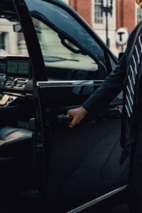 Person opening car door, dressed in formal attire with a striped tie.
