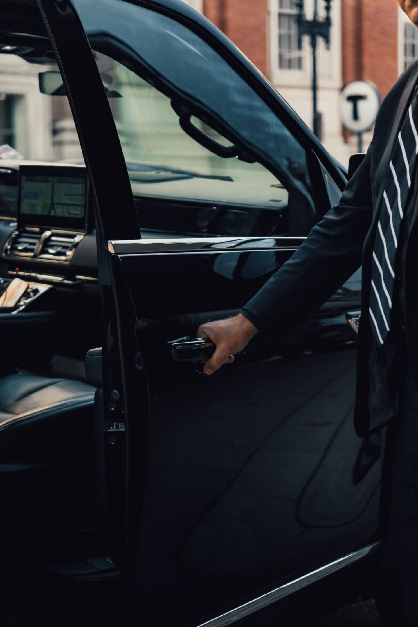 Person opening car door, dressed in formal attire with a striped tie.