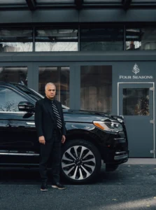 Man standing next to a black luxury SUV outside a building.