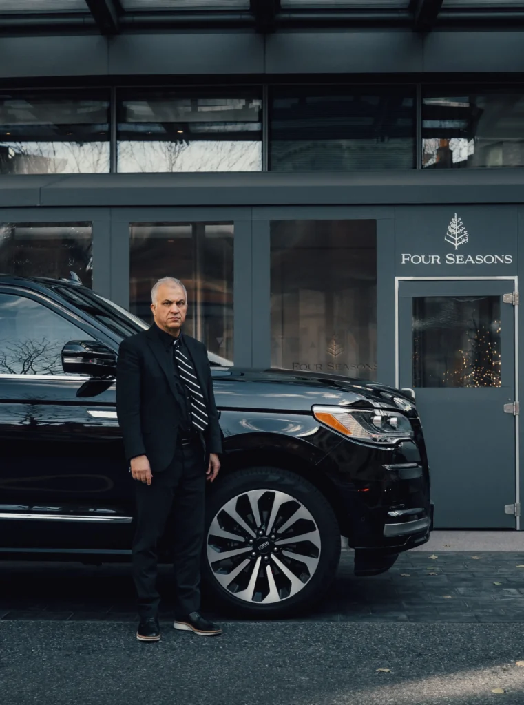 Man standing next to a black luxury SUV outside a building.