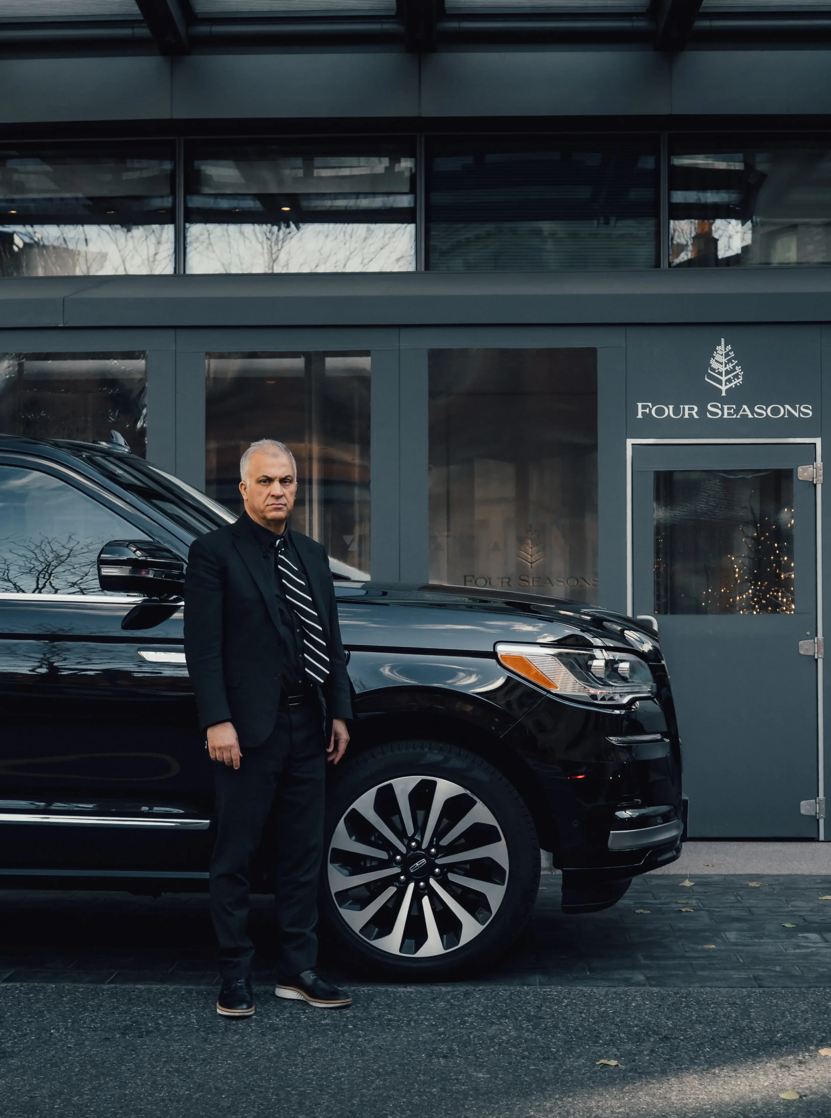 Man standing next to a black luxury SUV outside a building.
