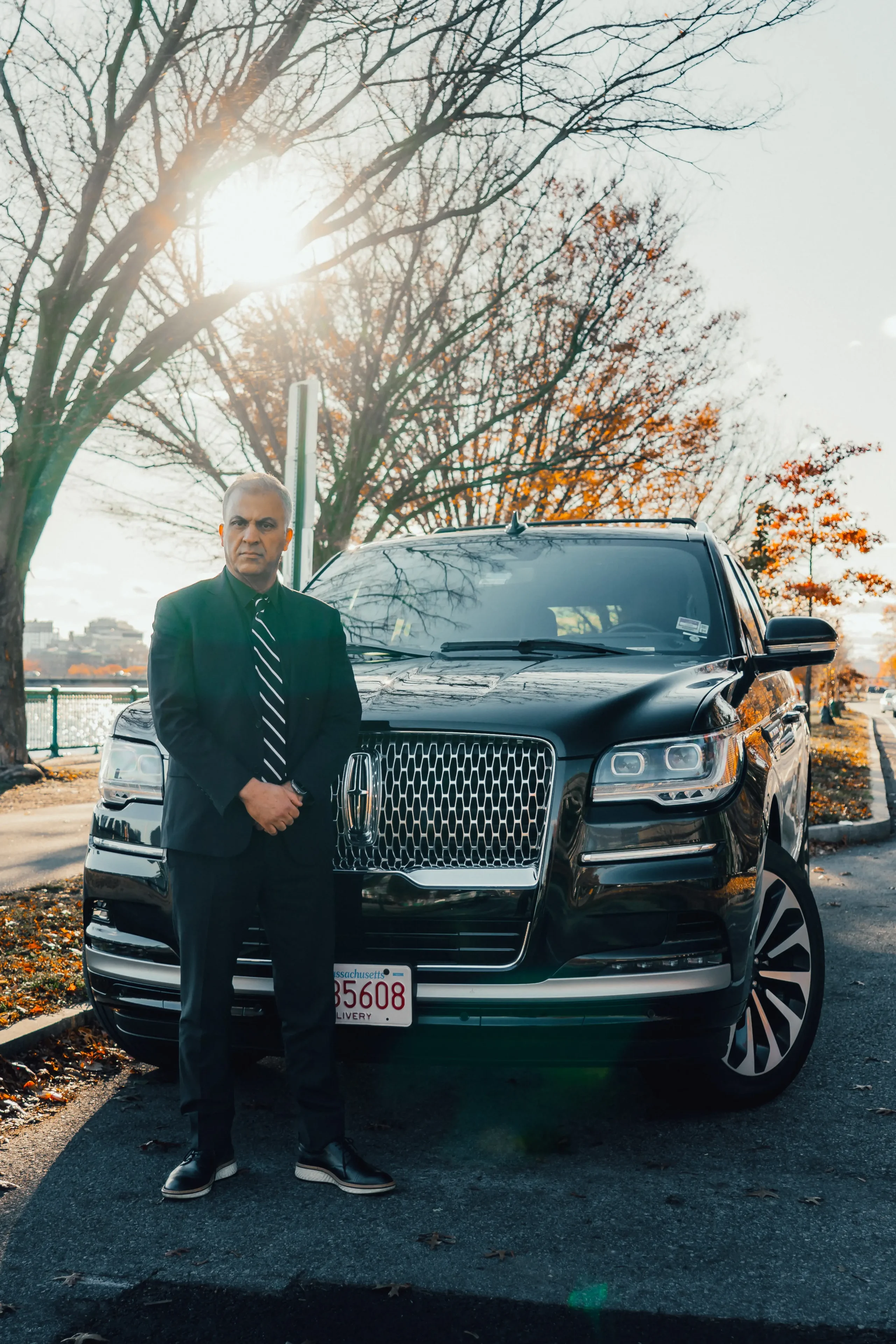 Chauffeur in black suit standing beside Lincoln Navigator near waterfront – Boston Limo VIP