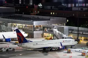 Delta Airlines aircraft parked at Logan Airport at night with terminal lights and ground vehicles