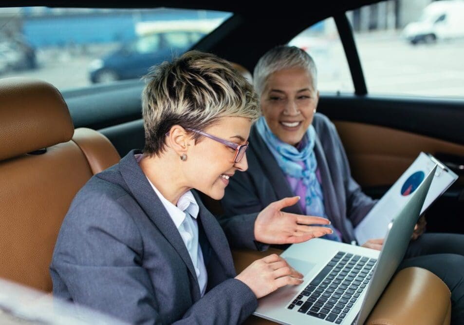 Two women sitting in a car looking at a laptop.